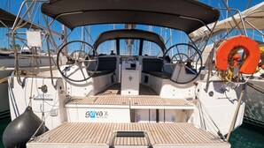 Dek van een boot met een stuurwiel, reddingsboei en een kombuisgedeelte.