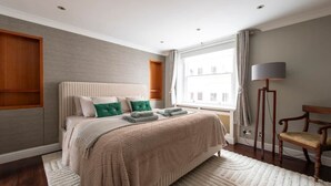 Ein Schlafzimmer mit einem Bett, einem Sessel, einer Lampe und einem Fenster.