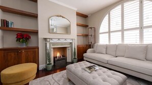 Ein Wohnzimmer mit Kamin, einer Couch, einem gelben Hocker und einem großen Bogenfenster.
