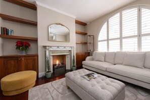 A living room with a fireplace, a sofa, a yellow ottoman, and a large arched window. - Prime Kensington Private Townhouse-Central London (London)