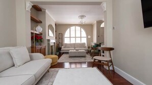 Ein Wohnzimmer mit einer Couch, Hocker und Sesseln, einem Kamin und einem großen Bogenfenster.