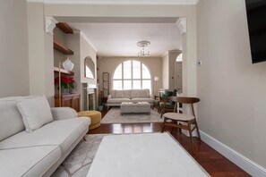 A living room with a sofa, ottoman, and chairs, a fireplace, and a large arched window. - Prime Kensington Private Townhouse-Central London (London)
