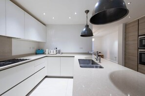A modern kitchen with white cabinetry, a stainless steel sink, and a black pendant light. - Prime Kensington Private Townhouse-Central London (London)