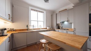 Una cocina moderna con armarios blancos, encimera de madera y dos taburetes de bar.