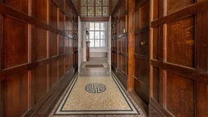 Un pasillo con paneles de madera, alfombra estampada y vista a una escalera.