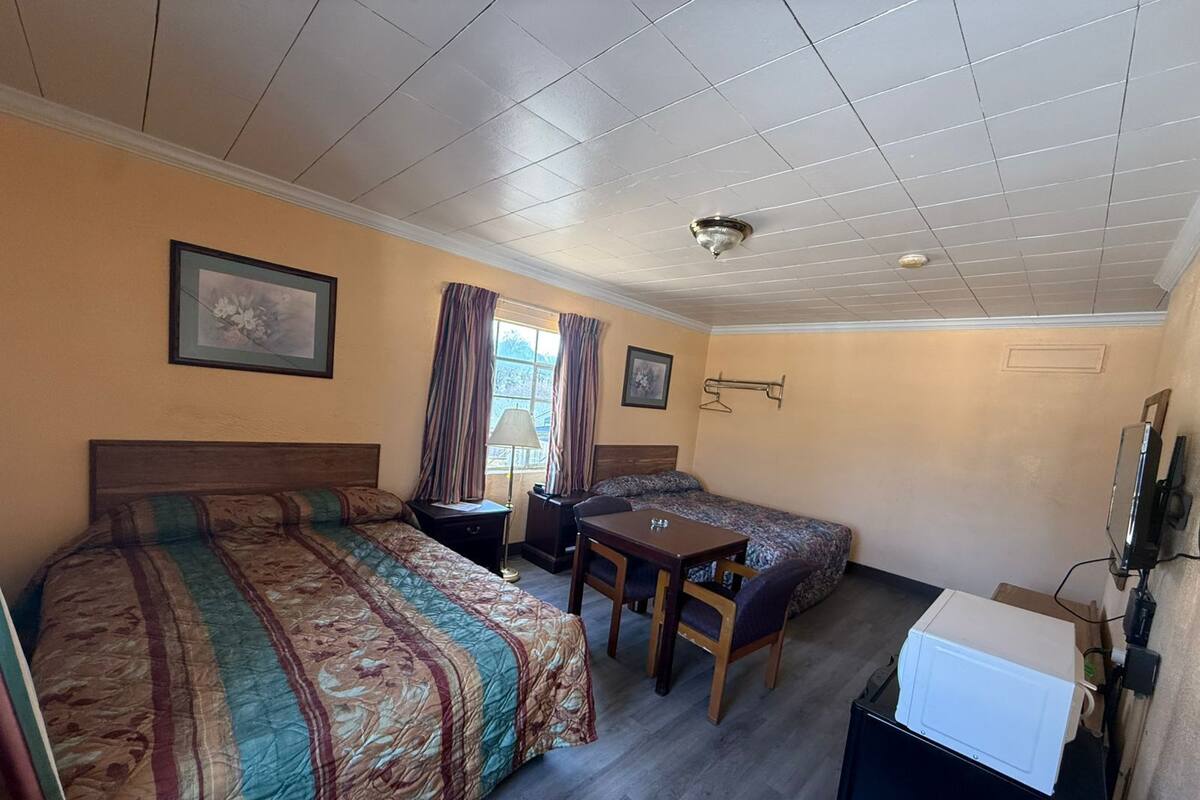 A room with two beds, a table, a chair, a TV, and a ceiling fan.