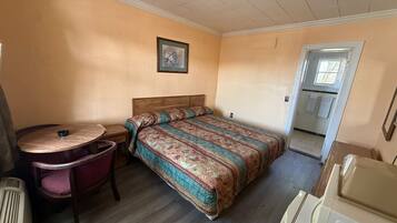 A small, single-room accommodation with a bed, a desk, a chair, and a radiator.