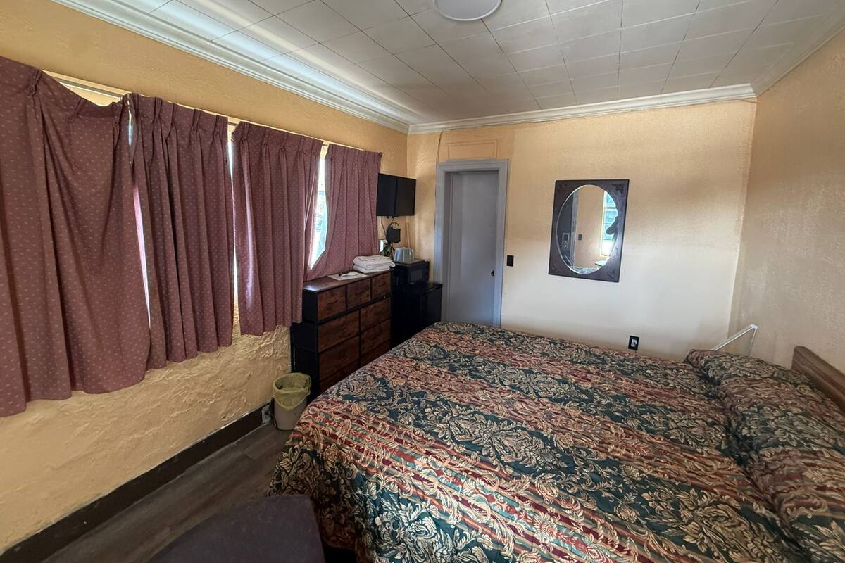 A bedroom with a bed, dresser, mirror, and a window with curtains.