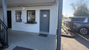 Un bâtiment avec une porte grise portant l’inscription « BUREAU », une fenêtre avec des stores et un petit auvent.