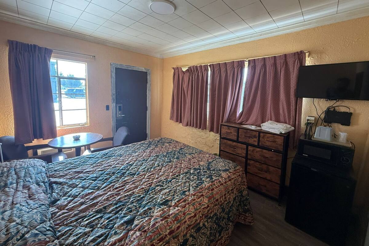 A room with a bed, a desk, a chair, a dresser, a television, and a window with curtains.