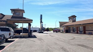 Un motel con una torre central, una estación de servicio y un estacionamiento con varios vehículos.