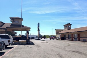 Un motel con una torre central, una estación de servicio y un estacionamiento con varios vehículos.