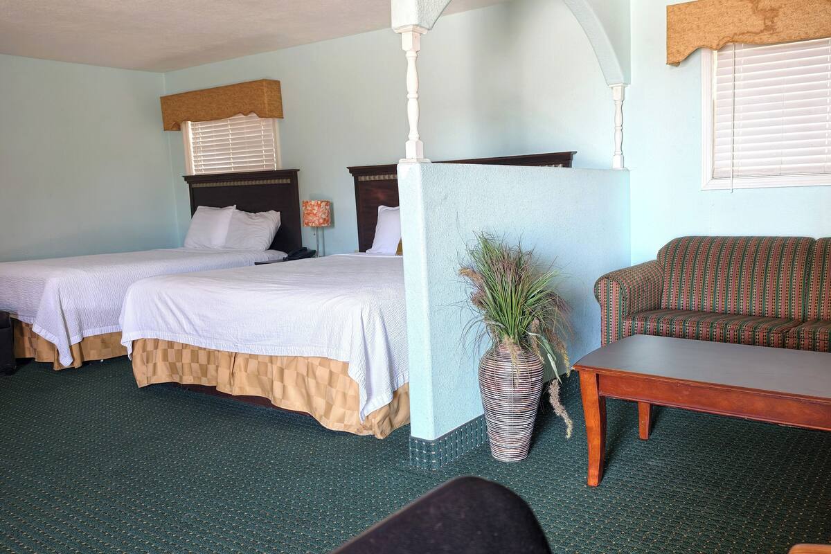 A room with two beds, a sofa, a wooden table, and a potted plant.