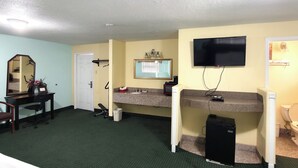 Habitación de hotel con escritorio, silla, espejo, televisión y un pequeño electrodoméstico negro.