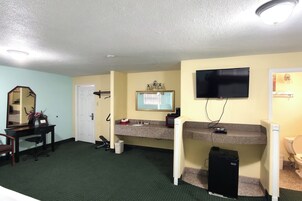 Habitación de hotel con escritorio, silla, espejo, televisión y un pequeño electrodoméstico negro.