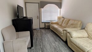 Una habitación con un sofá de cuero color crema, un mueble multimedia negro y un sillón blanco.