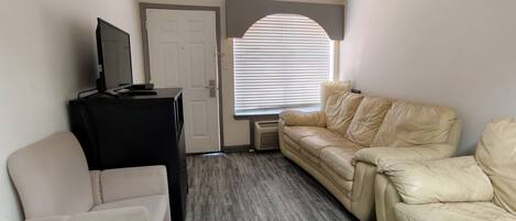 A room with a beige leather sofa, a black entertainment unit, and a white armchair.