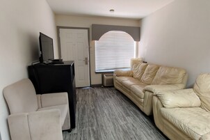 Una habitación con un sofá de cuero color crema, un mueble multimedia negro y un sillón blanco.