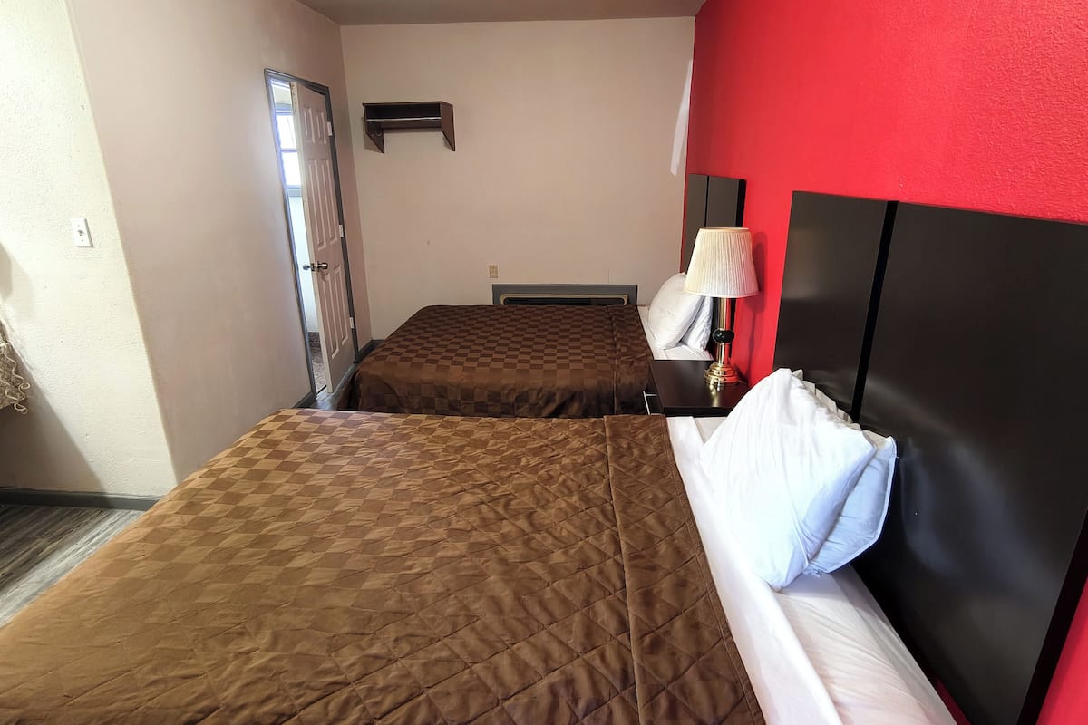A hotel room with two beds, a red wall, a black headboard, and a bedside lamp.