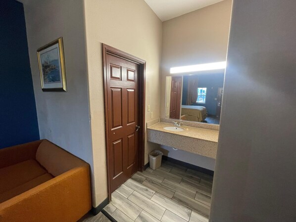 Une salle de bain avec une porte en bois, un lavabo, un miroir et une poubelle.