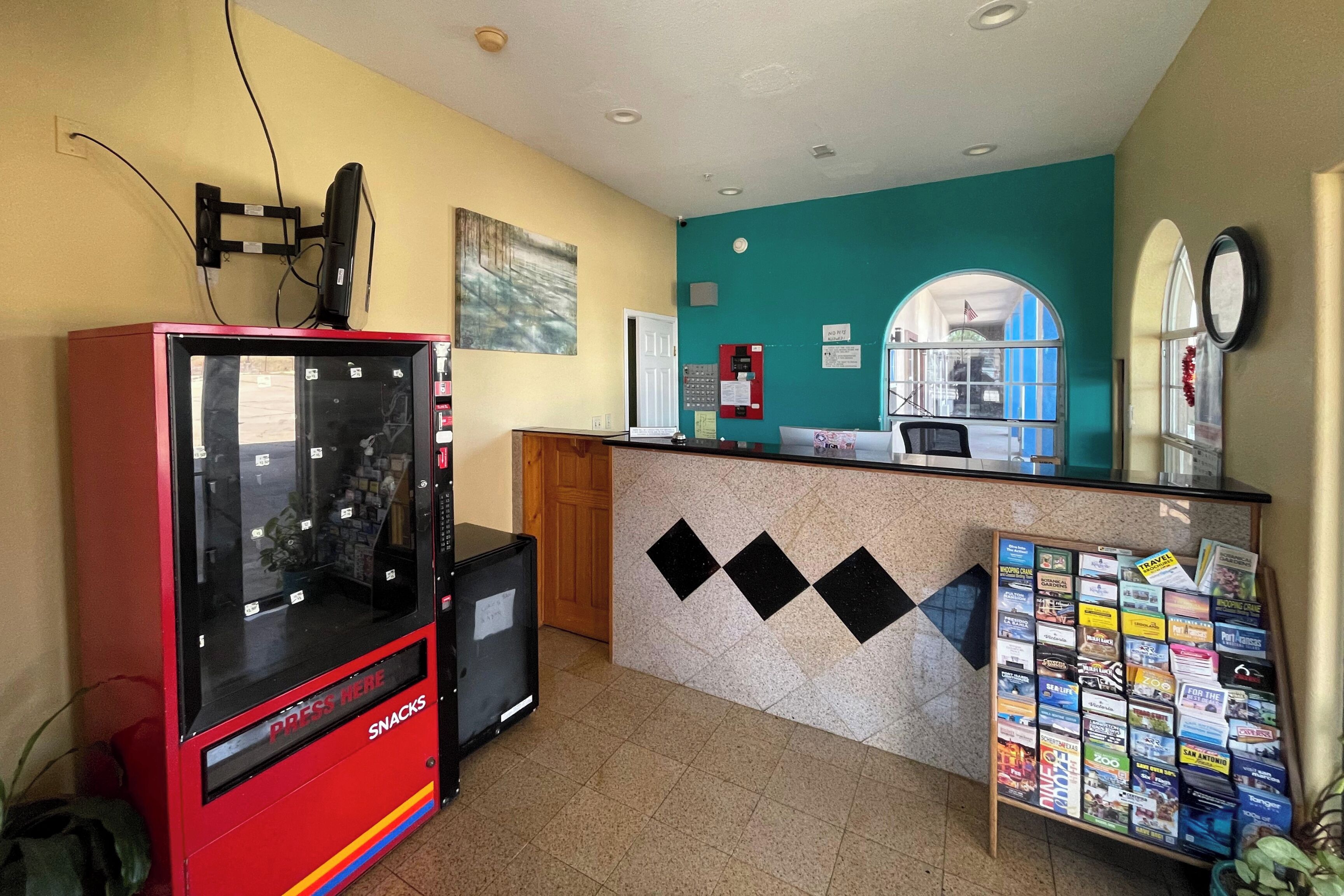 Aula, jossa on välipaloja myyvä automaatti, jonka kyltissä lukee ”VÄLIPALAT”, ilmoitustaulu, jossa on matkailuesitteitä, ja ikkuna, jossa on Yhdysvaltain lippu.
