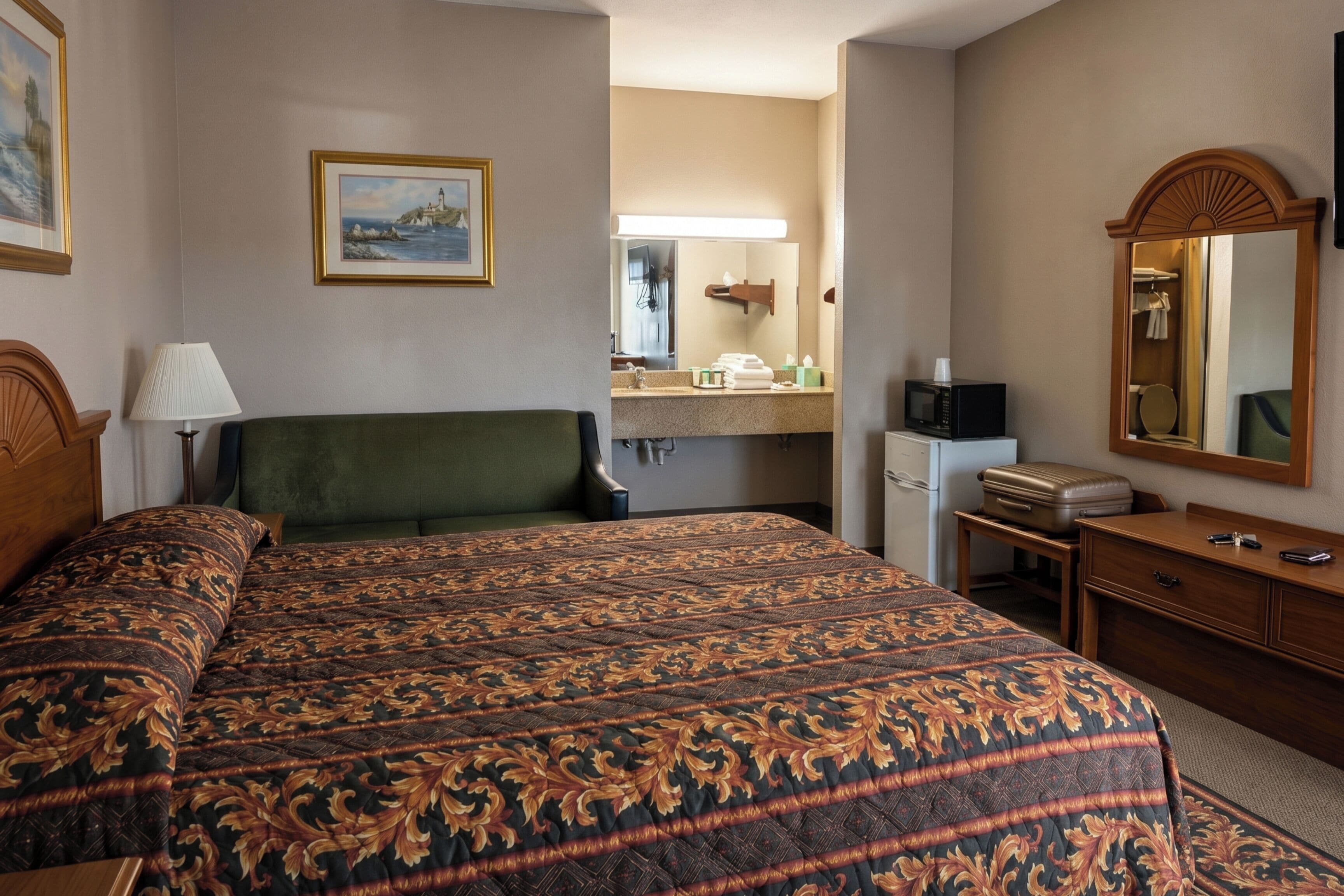 A hotel room with a large bed, a desk, a mirror, a microwave, and a small refrigerator.