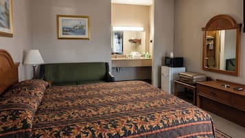 A hotel room with a large bed, a desk, a mirror, a microwave, and a small refrigerator.