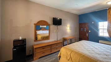 A hotel room with a bed, a television mounted on the wall, a dresser, a desk, and a window with curtains.