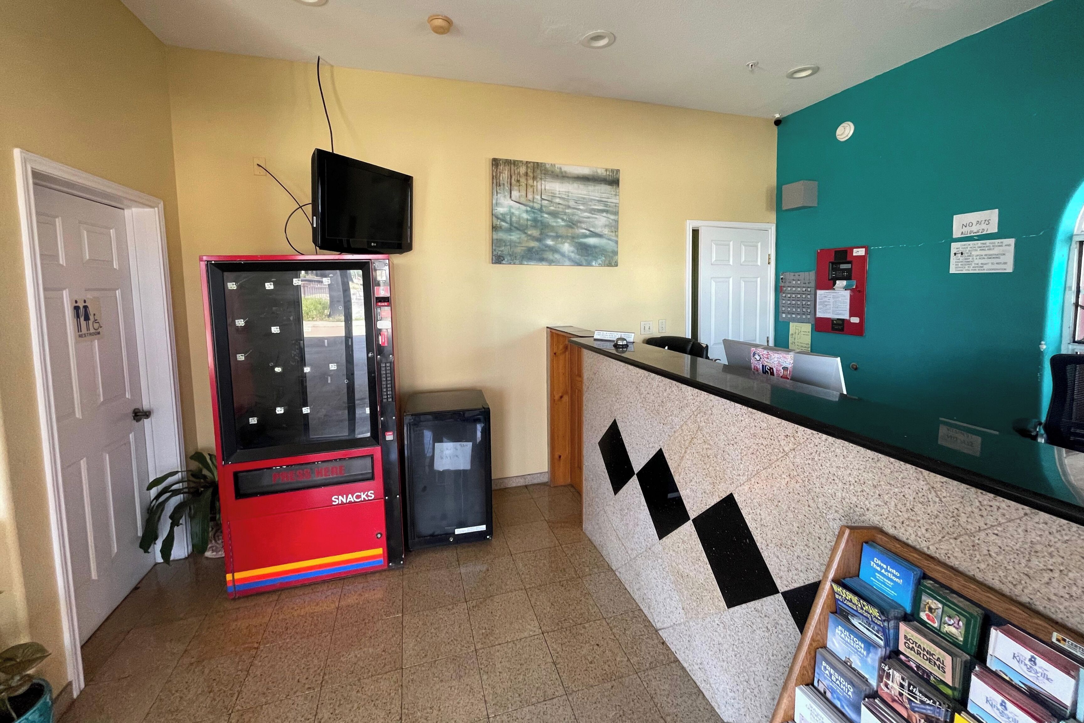 Un área de recepción con una máquina expendedora, un mostrador con una computadora y una pared decorada con un cuadro.
