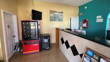 Un área de recepción con una máquina expendedora, un mostrador con una computadora y una pared decorada con un cuadro.