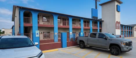 A building with a blue and red facade, a parking lot with marked spaces, and a grey pickup truck parked in one of the spaces.