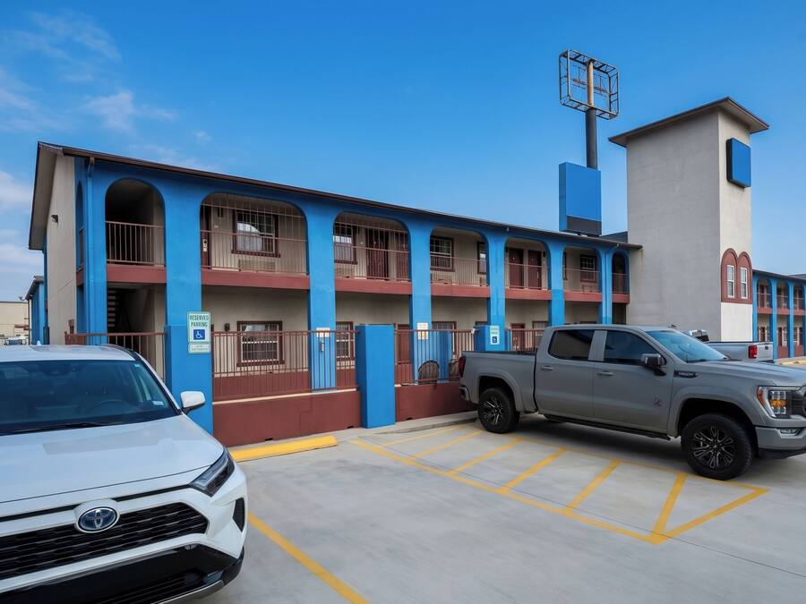 Een gebouw met een blauw-rode gevel, een parkeerplaats met aangegeven plekken, en een grijze pick-up truck geparkeerd in een van de plekken.