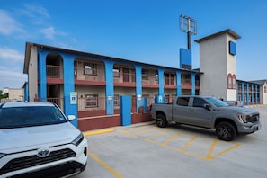 A building with a blue and red facade, a parking lot with marked spaces, and a grey pickup truck parked in one of the spaces. - Airport Inn & Suites South Padre Island I 37 (Corpus Christi)