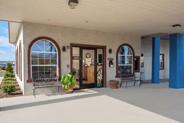 A building with a covered entrance, arched windows, and a door with signage. - Airport Inn & Suites South Padre Island I 37 (Corpus Christi)