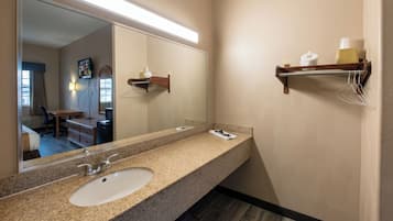 A bathroom with a granite countertop sink, a mirror, a towel rack, and a shelf with toiletries.