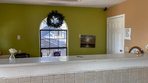 A reception area with a green wall, a window with a wreath, a painting, and a sign on the door. - Deluxe Inn & Suites Corpus Christi I 37 (Corpus Christi)
