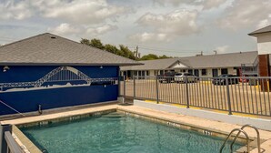 A swimming pool with a blue wall and a bridge mural, surrounded by a fence and a parking area. - Deluxe Inn & Suites Corpus Christi I 37 (Corpus Christi)