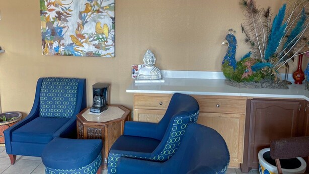 A room with two blue chairs, a coffee maker, a Buddha statue, and a peacock decoration. - Deluxe Inn & Suites Corpus Christi I 37 (Corpus Christi)