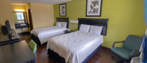 Ett hotellrum med två sängar, ett skrivbord, en stol, ett badrum och en grön vägg.