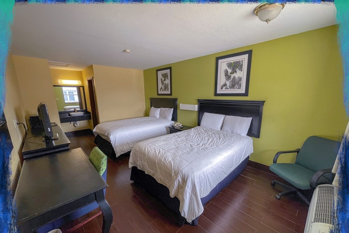 Una habitación de hotel con dos camas, un escritorio, una silla y un baño a la vista.