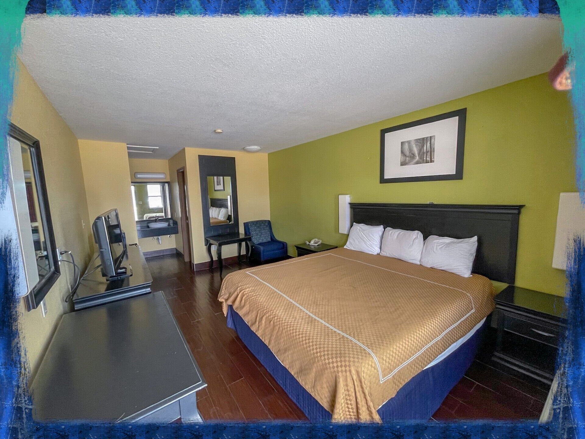 A hotel room with a bed, bedside table, chair, desk, and a mirror.
