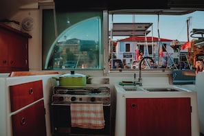 A compact kitchen with a stove, sink, and window overlooking a street scene. - Sun-Kissed Sailing: A Luxurious Beach Experience in Nikiti, Macedonia (Nikiti)