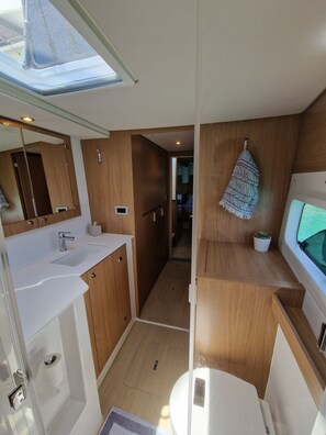 Une salle de bain compacte pour camping-car, dotée d'un puits de lumiÚre, d'un lavabo, de toilettes et d'un miroir.