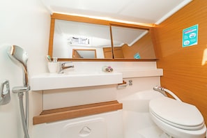 A bathroom with a white sink, mirror, and toilet, wooden paneling, and a shower.