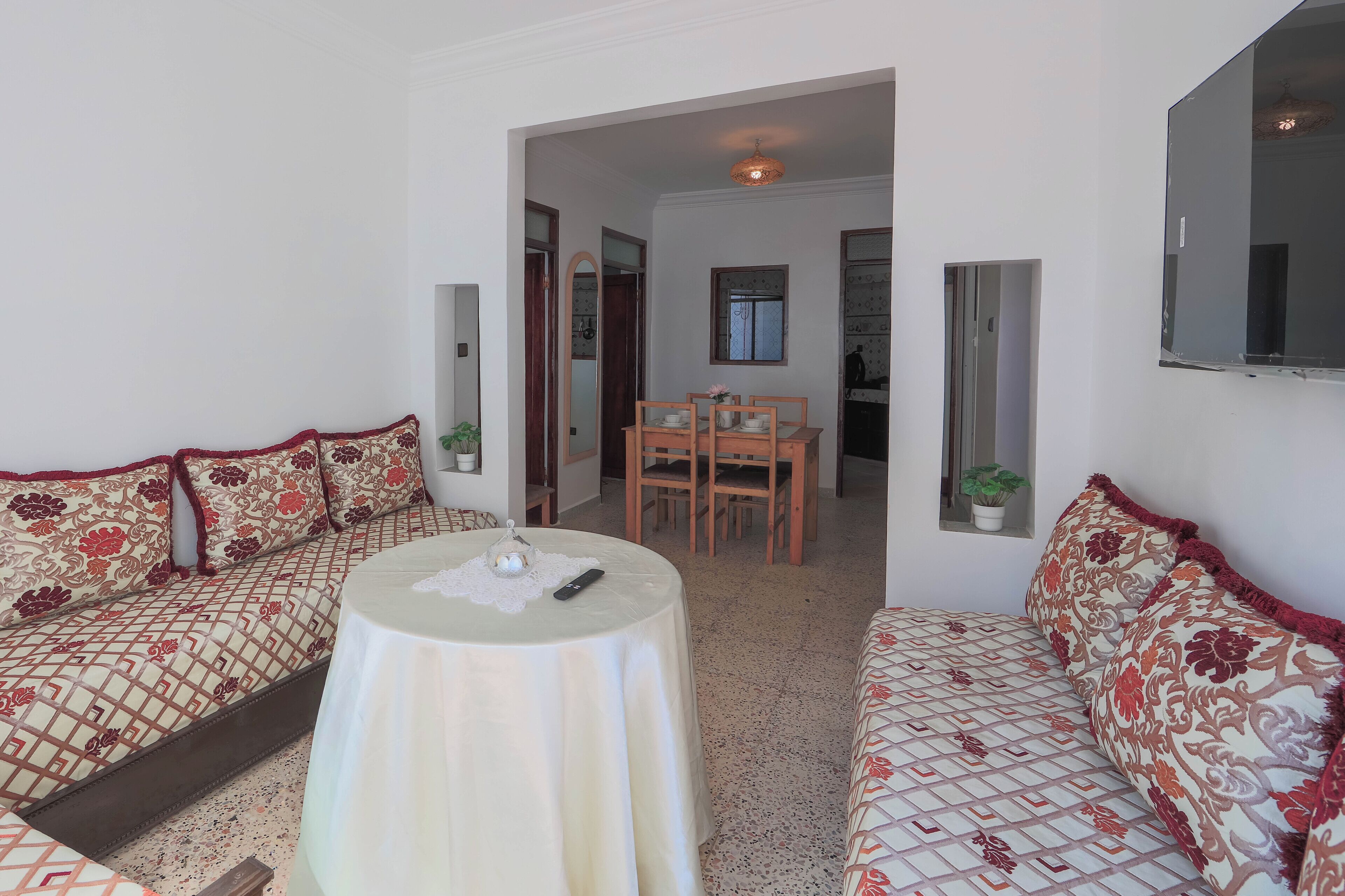 A room with a sofa, a round table, and a dining area with chairs and a small plant.