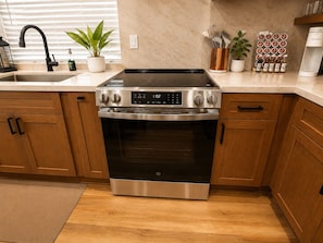 Una cocina con estufa de acero inoxidable, armarios de madera, un lavabo y una planta en maceta.