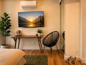 A cozy room with a wooden table, a black chair, a potted plant, a framed picture, and a small dog.