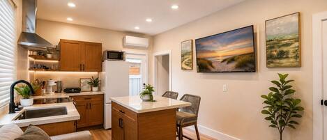 A compact kitchen with wooden cabinets, a microwave, and a refrigerator. There is a dining area with a table and chairs, and a potted plant.