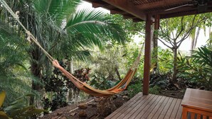 Uma rede pendurada em uma estrutura de madeira em um jardim exuberante, com um deck de madeira e uma pequena mesa.