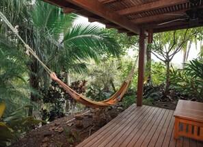Eine Hängematte, die an einer Holzkonstruktion in einem üppigen Garten befestigt ist, mit einer Holzdielen-Terrasse und einem kleinen Tisch.